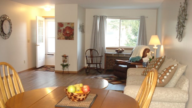 A dining area with a wooden table and chairs, a fruit basket, and a sofa with patterned cushions.