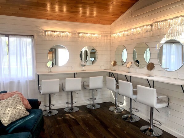 Un salón con varios espejos y sillas blancas, techo de madera y una ventana con cortinas.