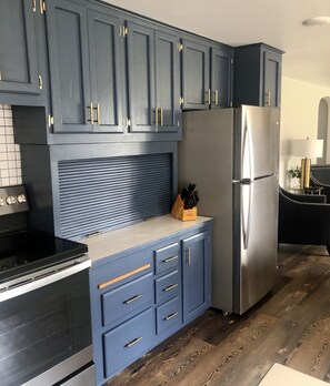 Una cocina con armarios azul oscuro, un refrigerador de acero inoxidable y una estufa negra.