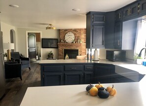 Una cocina moderna con armarios oscuros, una isla grande, una chimenea de ladrillo y un reloj encima.