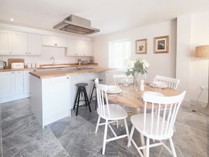 A modern kitchen with white cabinetry, a wooden island, and a dining area with white chairs and a wooden table. - The Old Stables 3 - UK35690 (Winterslow, near Salisbury)