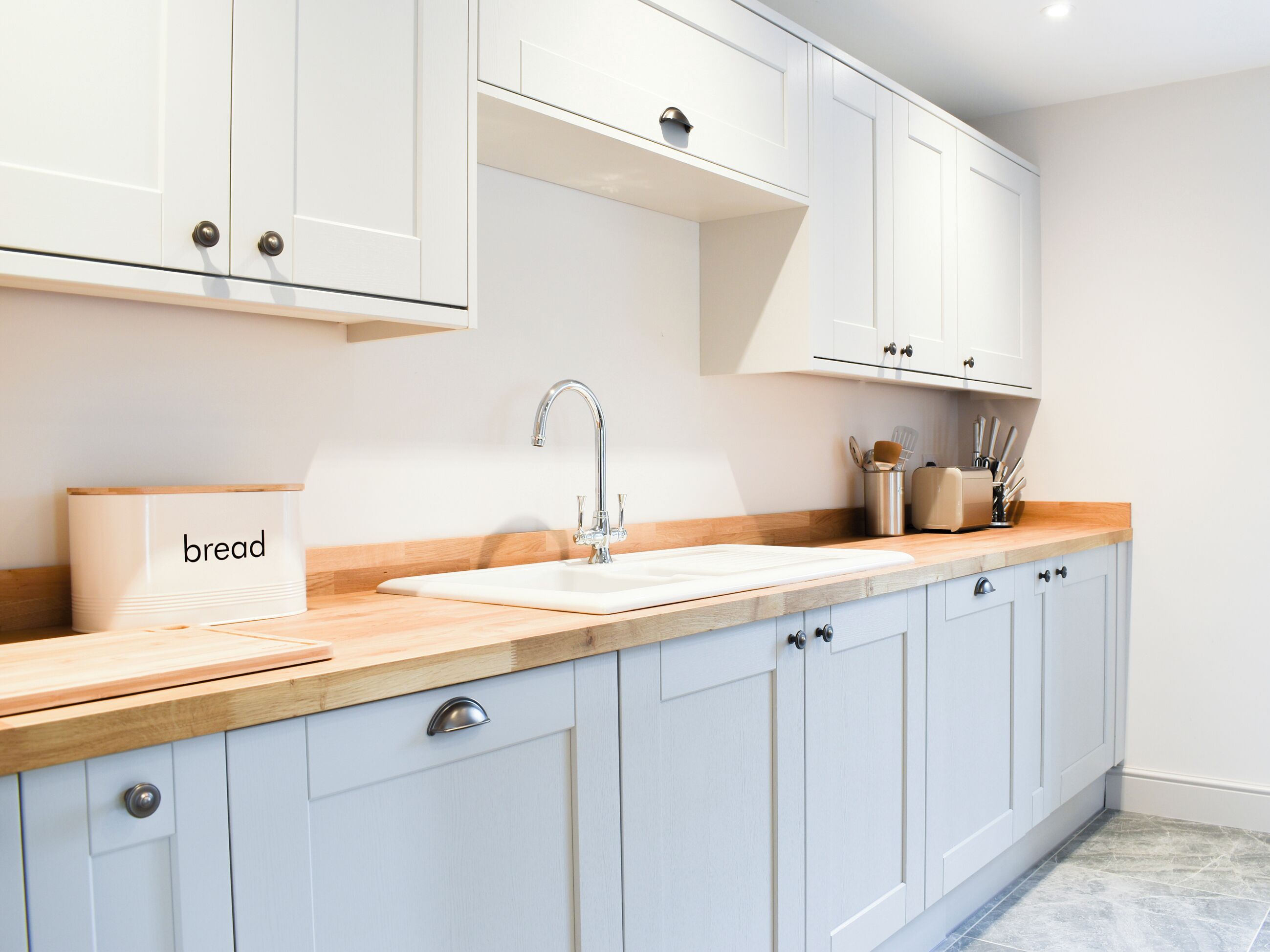 A modern kitchen with white cabinets, a wooden countertop, a sink, and a bread container.