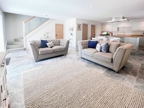 A spacious living area with two beige sofas, a large woven rug, and a kitchen in the background. - The Old Stables 3 - UK35690 (Winterslow, near Salisbury)