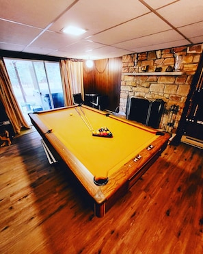Een pooltafel in een ruimte met houten vloeren, een stenen muur en een raam met gordijnen.