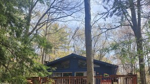 A two-story cabin with a deck, surrounded by trees.