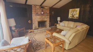 A cozy living room with a stone fireplace, a sofa, a wicker chair, and a wooden coffee table.