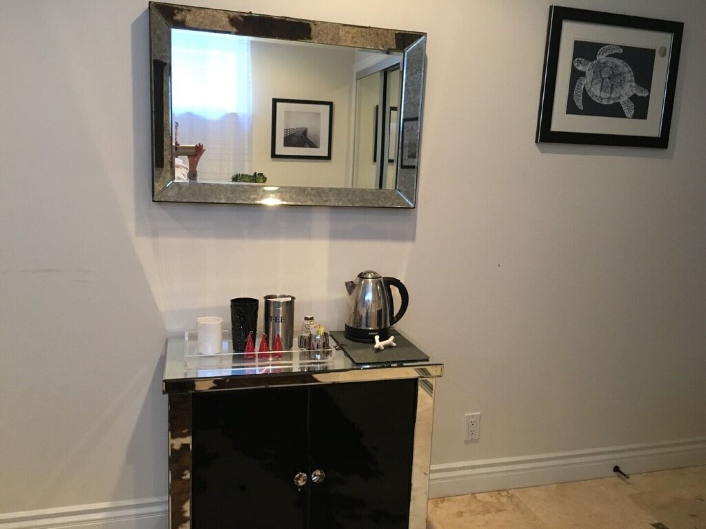 A kitchen area with a countertop, a kettle, and a coffee maker. There is a framed picture of a turtle on the wall.