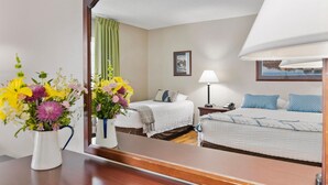 A hotel room with two beds, a bedside table with a lamp, a mirror, and a vase of flowers.