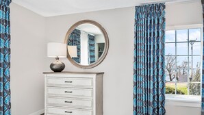 Une pièce avec une commode blanche, un miroir rond et des rideaux à motifs bleus.
