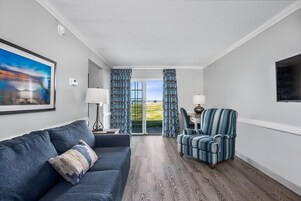 Una sala moderna con sofá, sillón y vistas al exterior a través de un ventanal.