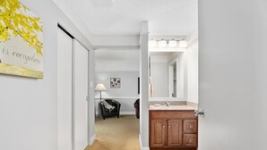 A hallway leading to a bathroom with a vanity, a mirror, and a door. - Top Floor Master Suite Bay View (North East)