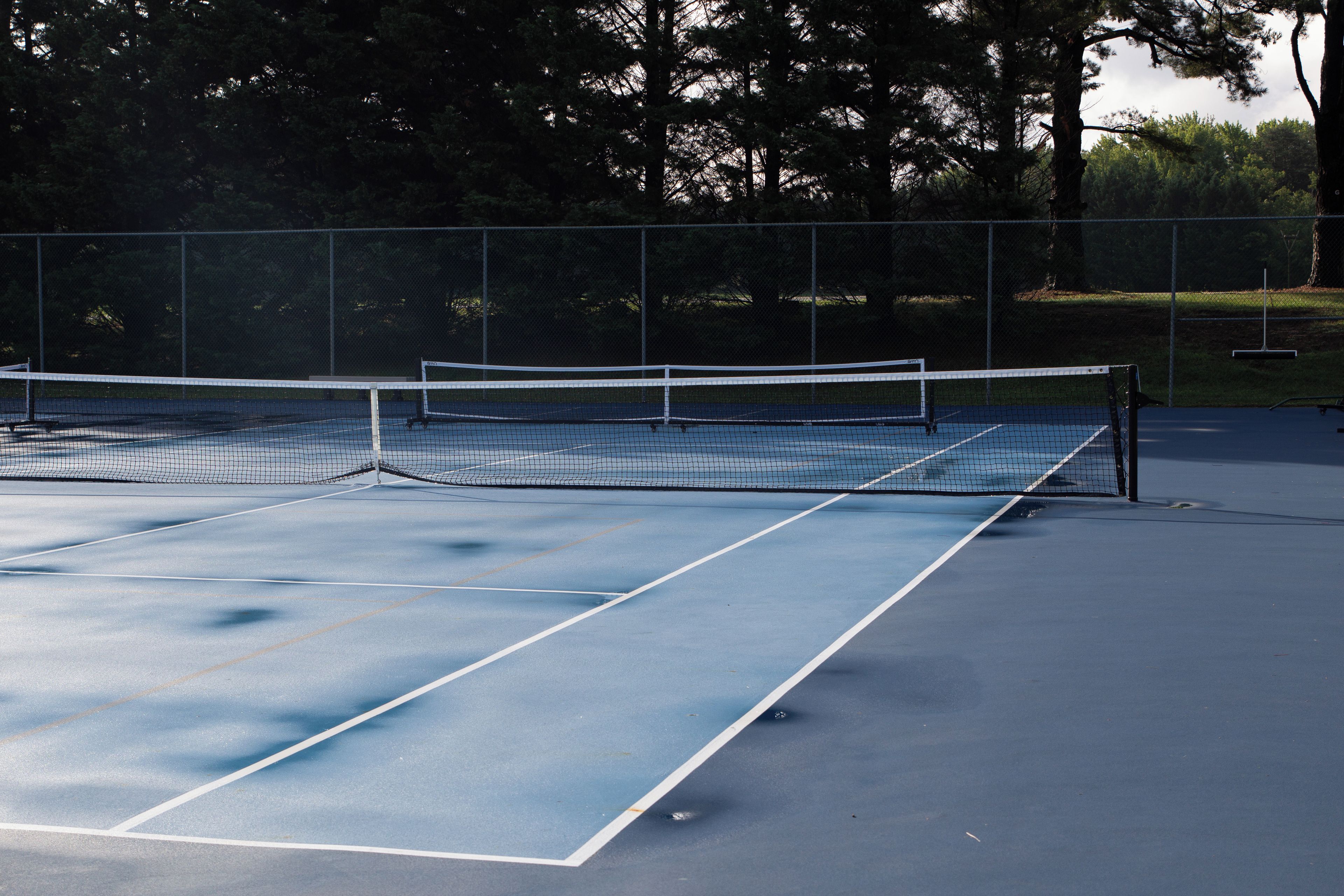 A tennis court with a net, surrounded by a fence and trees.