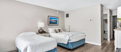 Habitación de hotel con dos camas, una mesita de noche, una lámpara y un cuadro en la pared.