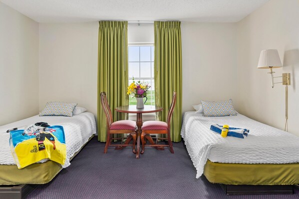 A hotel room with two beds, a small round table with chairs, a vase with flowers, and a lamp. - First Floor Standard Deluxe Bay View (North East)