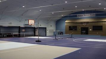 An indoor sports facility with a basketball court, a volleyball net, and a sign reading 'Jesus Never Fails'.