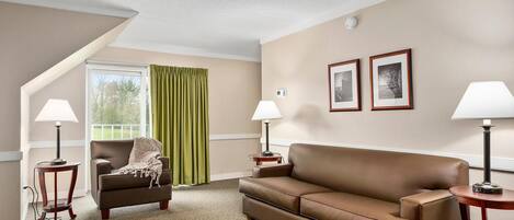 A hotel room with a brown leather sofa, two side tables with lamps, a green curtain, and two framed pictures on the wall.
