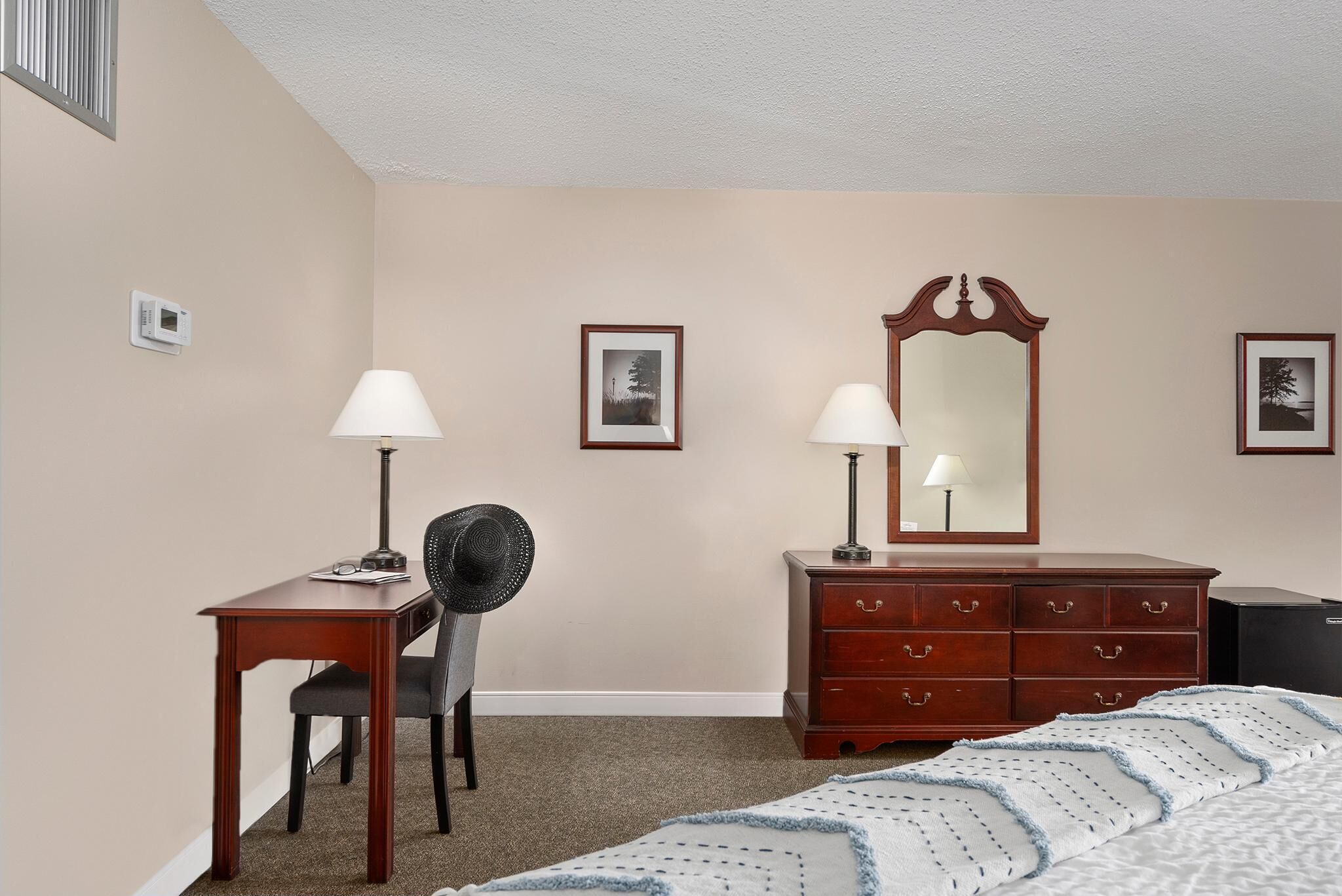 A bedroom with a bed, a desk, a chair, a dresser, and two wall-mounted lamps.