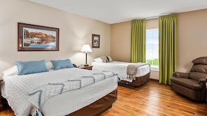 A hotel room with two beds, a reclining chair, a window with green curtains, and a painting on the wall. - Top Floor Handicap Accessible Bay View (North East)