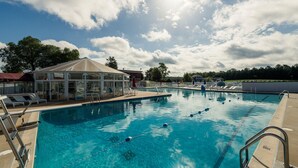A swimming pool with clear blue water, surrounded by lounge chairs and a covered seating area.