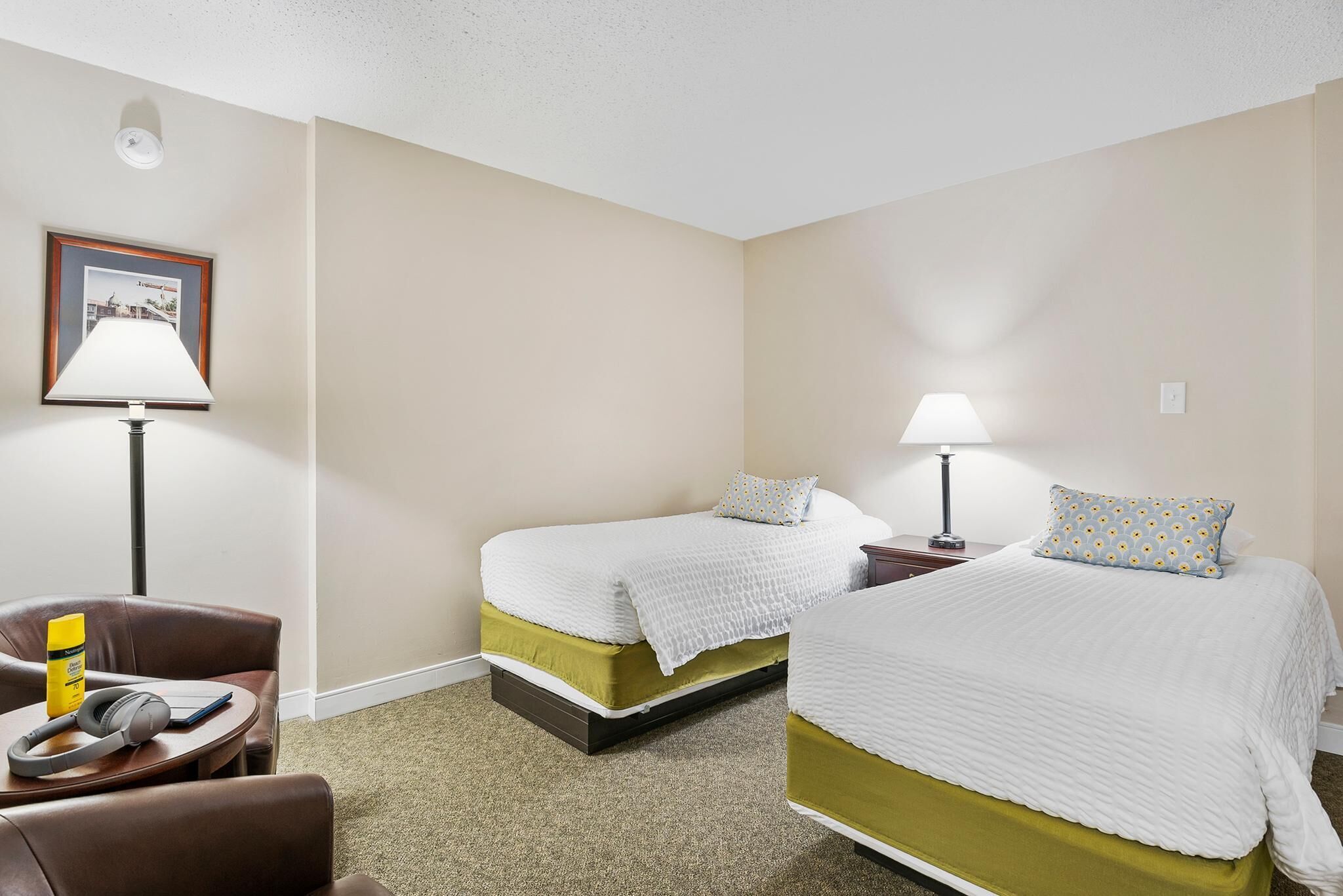 Une chambre d’hôtel avec deux lits simples, un bureau, une chaise et une lampe.