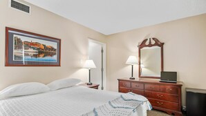 A hotel room with a bed, a dresser, a mirror, a lamp, and a framed picture on the wall.