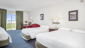 A hotel room with three beds, a desk with a chair, a window with curtains, and two wall-mounted lamps. - Second Conference Family Deluxe Bay View (North East)