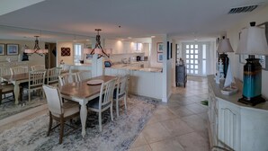 A spacious kitchen with a central island, a dining area with a wooden table and chairs, and a living area with a large window. - Penthouse level with Beach View 2 Bedroom Condo (Longboat Key)