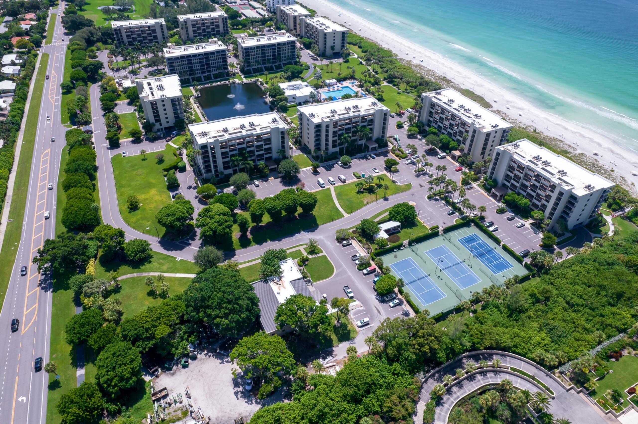An aerial view of a coastal residential area with multiple high-rise buildings, a beach, and a tennis court.