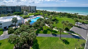 A resort with a pool, palm trees, and a view of the ocean. - Penthouse level with Beach View 2 Bedroom Condo (Longboat Key)
