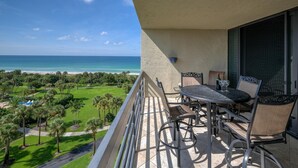 A balcony with a table and chairs overlooking a beach and pool area. - Penthouse level with Beach View 2 Bedroom Condo (Longboat Key)