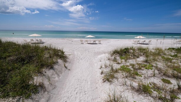 A beach with white sand, clear blue water, and three white umbrellas. - Penthouse level with Beach View 2 Bedroom Condo (Longboat Key)
