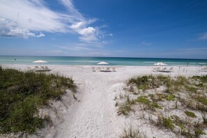 Uma praia com areia branca, águas azul-claras e três guarda-sóis brancos.
