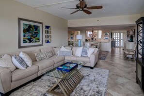 A spacious living room with a beige sofa, a glass coffee table, and a ceiling fan. - Penthouse level with Beach View 2 Bedroom Condo (Longboat Key)