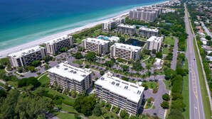 An aerial view of a coastal hotel complex with multiple buildings, a beach, and a road. - Penthouse level with Beach View 2 Bedroom Condo (Longboat Key)