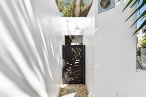 A narrow white corridor with a black decorative gate, leading to a building entrance.