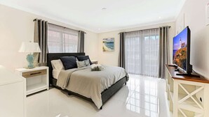 A modern bedroom with a bed, nightstands, a TV, and a large window. - Seahorse Villa 1 By Dream Vacation (Fort Lauderdale)