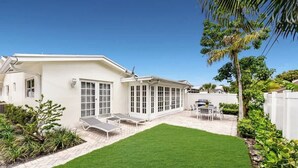 A house with a white exterior, a covered patio with seating, a well-maintained lawn, and a palm tree. - Seahorse Villa 1 By Dream Vacation (Fort Lauderdale)