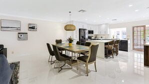 A modern kitchen with white cabinets, a central island, and a dining area with a table and chairs. - Seahorse Villa 1 By Dream Vacation (Fort Lauderdale)