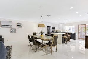 Une cuisine moderne avec des meubles blancs, un îlot central et un coin repas comprenant une table et des chaises.