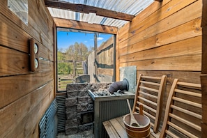 A rustic wooden room with a large window, a wooden bench, a metal container, and a wooden ladder.