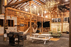 Een rustiek houten interieur met een hoge plafond, sfeerverlichting, een hangmat, een grill en een picknicktafel.