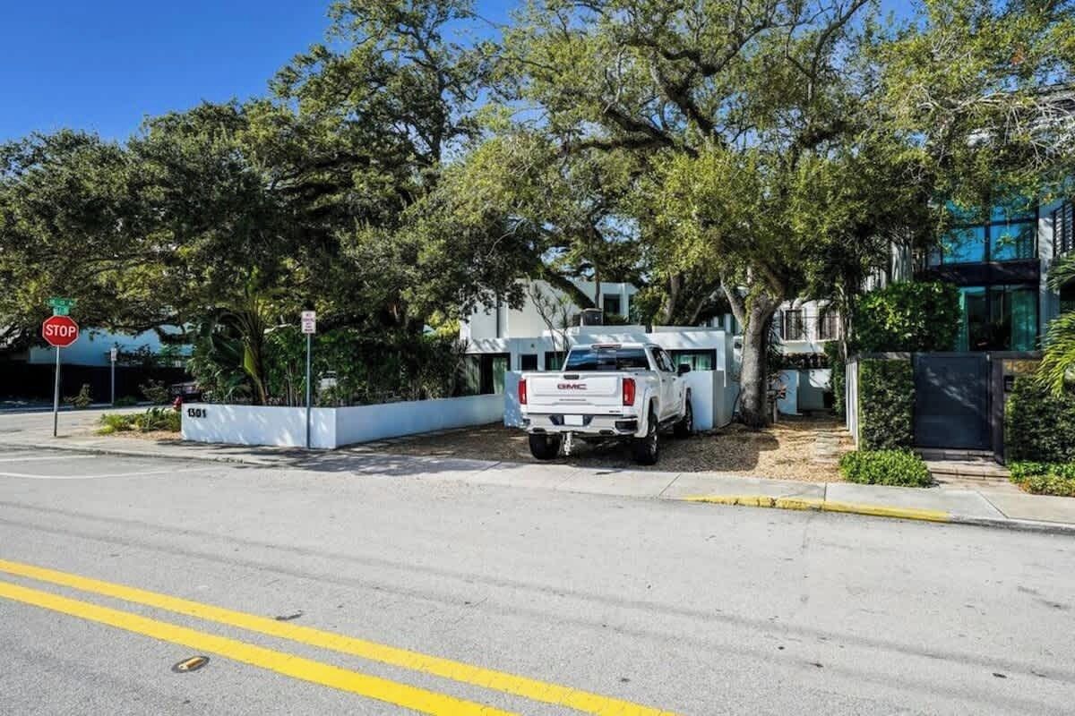 Un camion blanc est garé à un panneau d’arrêt, un bâtiment à l’architecture moderne se dresse à proximité, et une rue bordée d’arbres s’étend devant nous.