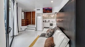 Een moderne woonkamer met een witte bank, een keuken op de achtergrond en een trap naar een hoger niveau.
