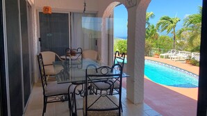 Een glazen balkon met een zwembad, buitenmeubels en uitzicht op de oceaan.