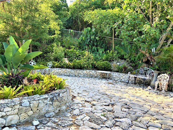 A garden with a stone pathway, a metal bench, and various plants.