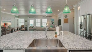 A spacious kitchen with a large island, stainless steel appliances, and hanging green pendant lights. - The Oceanic, Beachfront Oasis*Sleeps 20*Hot Tub (Crystal Beach)