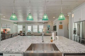 A spacious kitchen with a large island, stainless steel appliances, and hanging green pendant lights. - The Oceanic, Beachfront Oasis*Sleeps 20*Hot Tub (Crystal Beach)