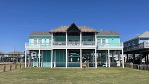 A two-story building with a thatched roof, a balcony on the upper floor, and a covered area with a railing. - The Oceanic, Beachfront Oasis*Sleeps 20*Hot Tub (Crystal Beach)
