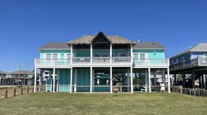 A two-story building with a thatched roof, a balcony on the upper floor, and a covered area with a railing. - The Oceanic, Beachfront Oasis*Sleeps 20*Hot Tub (Crystal Beach)