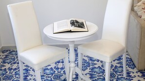 A small white table with an open book on it, flanked by two white chairs, set on a blue patterned floor. - King Room with Balcony (Sorrento)